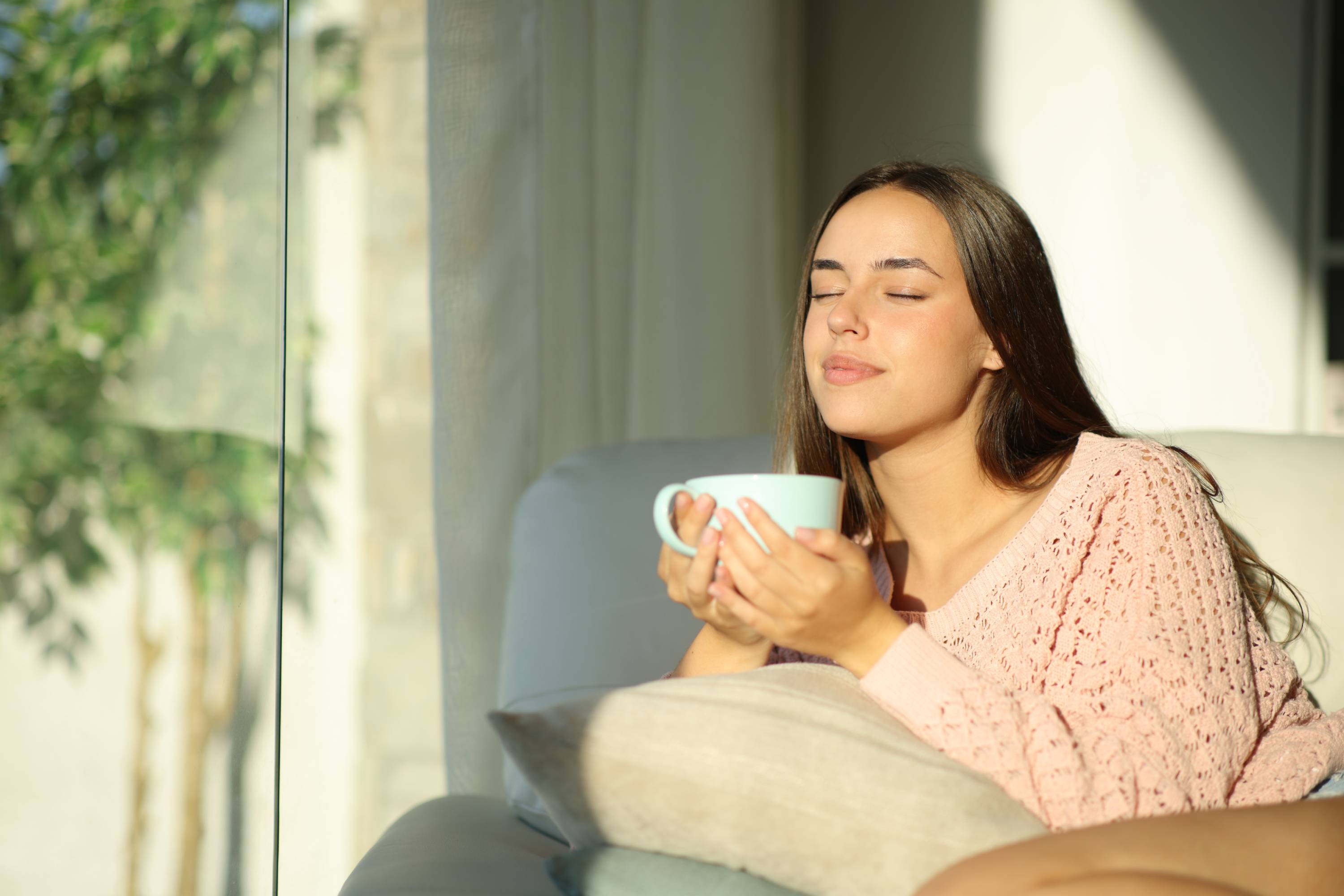 Junge Frau entspannt auf dem Sofa, hält eine hellblaue Tasse in der Hand