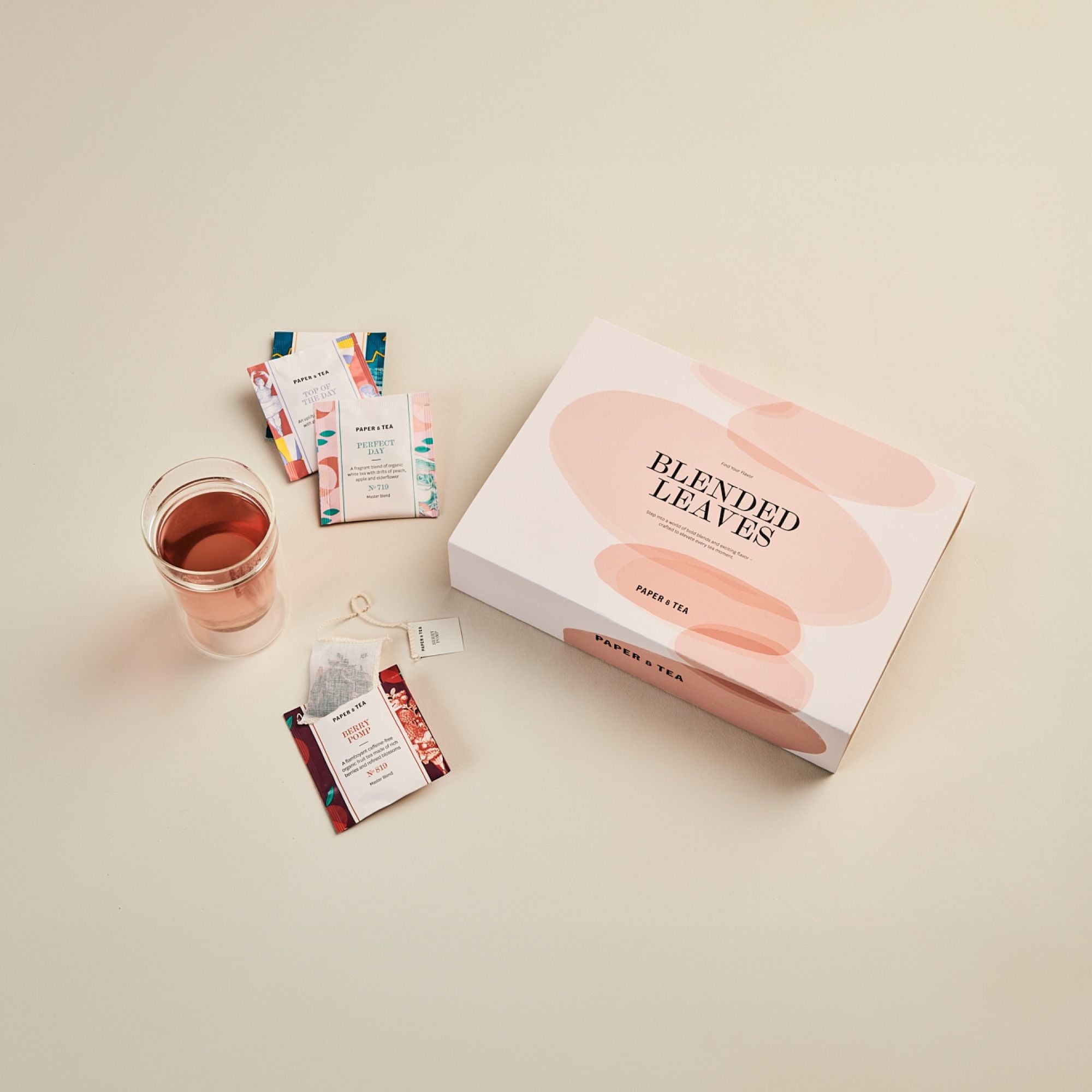 Pastellfarbene BLENDED LEAVES Teebox von PAPER & TEA mit buntem Tee und rosa Getränk.