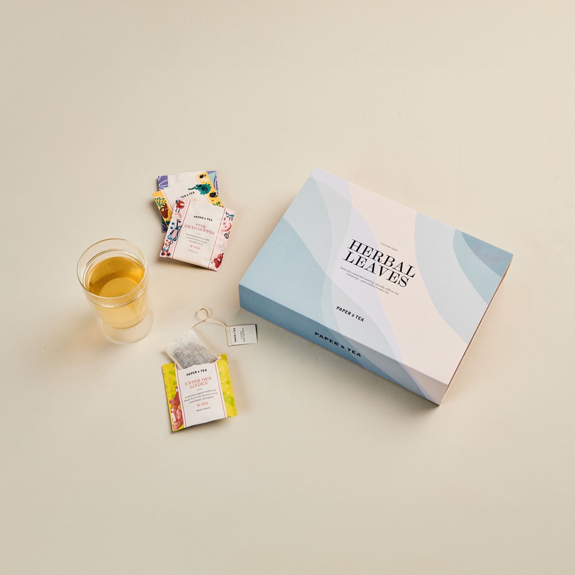 Stilvoll arrangierte Paper & Tea Kräutertees mit Teedose, Pink Grasshopper, Unter den Linden und Teetasse.