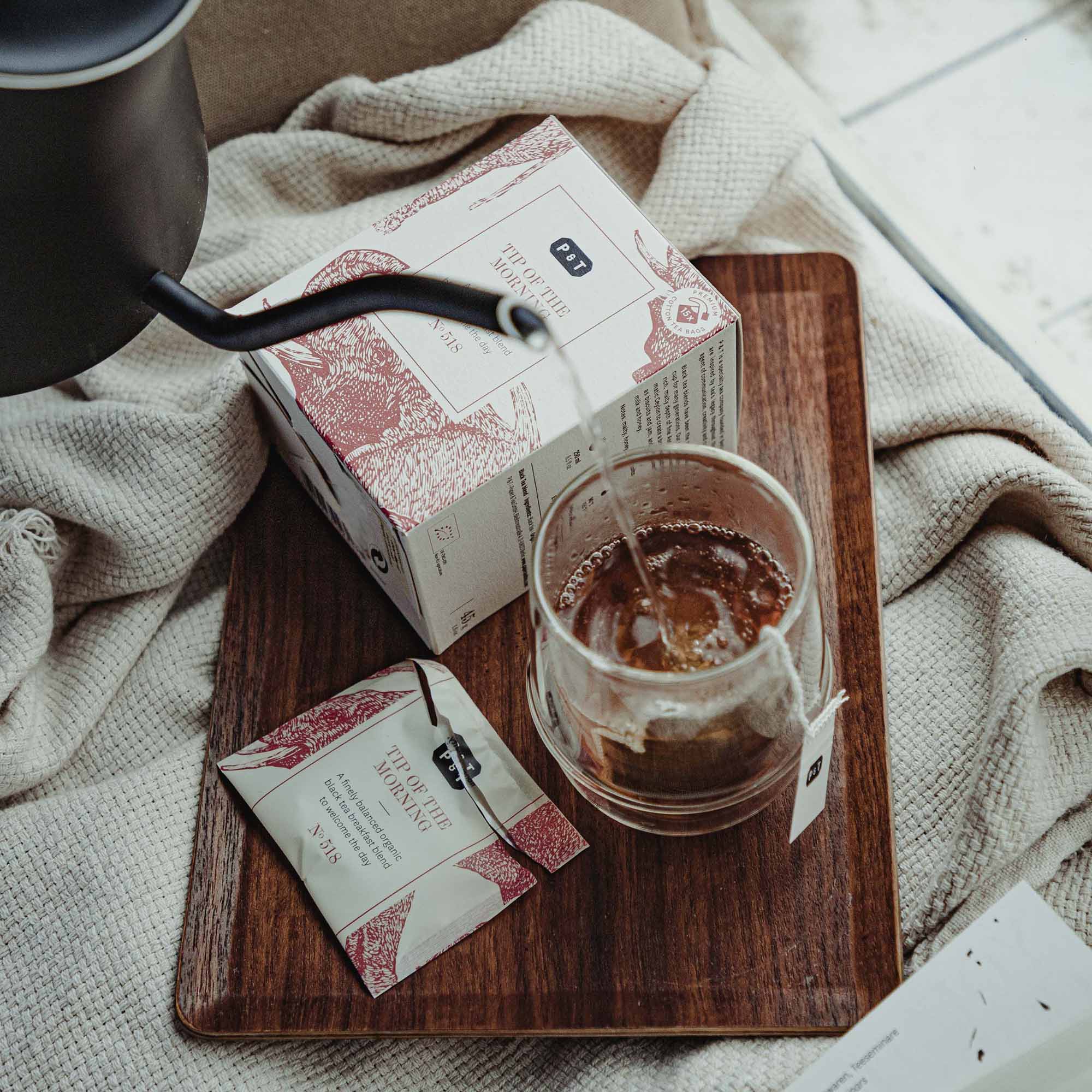 Holztablett mit Bio-Schwarztee "TIP OF THE MORNING," Tee wird aus Kanne in Glastasse gegossen.