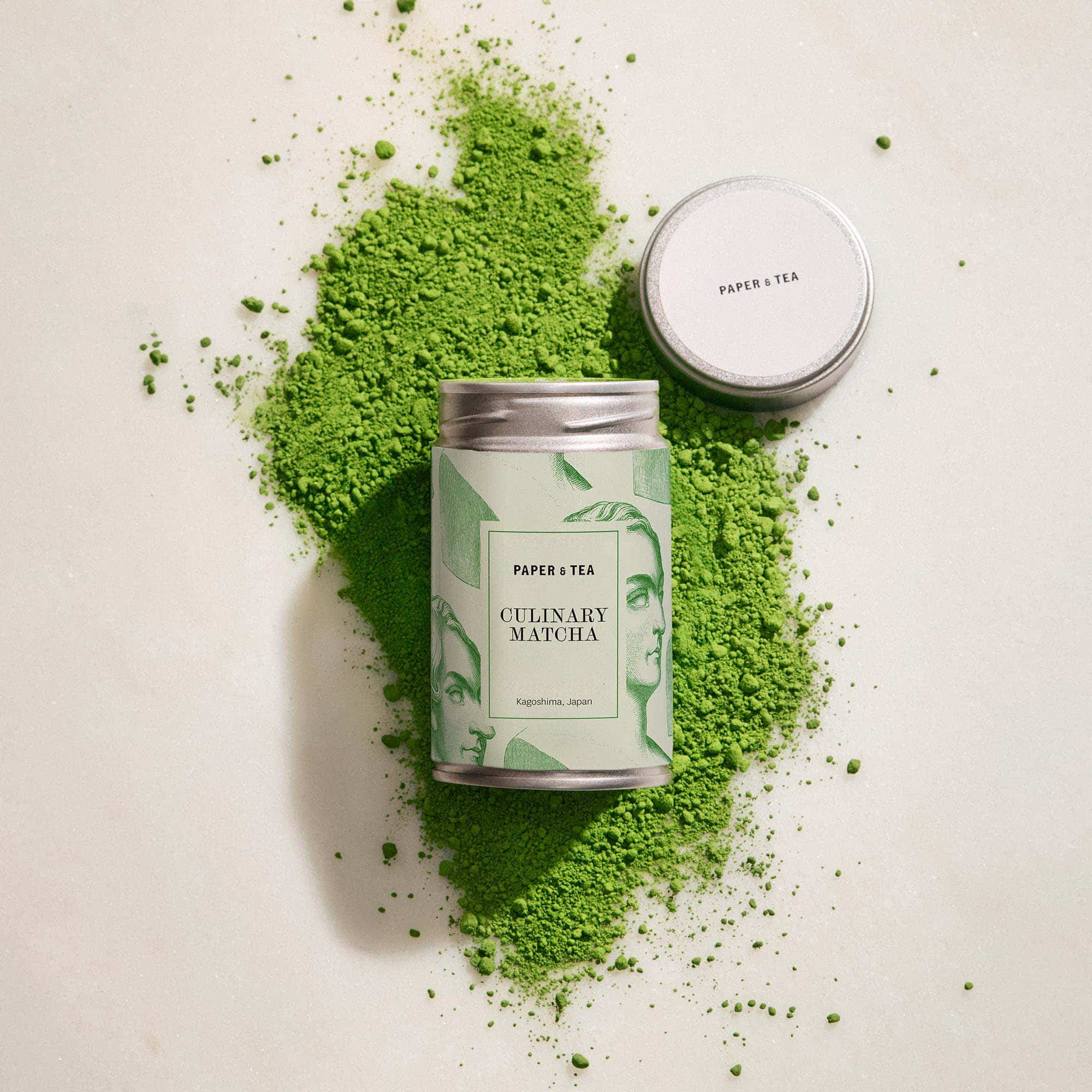 Silberne Dose mit künstlerischem Etikett für PAPER & TEA Culinary Matcha aus Kagoshima, umgeben von grünem Matcha-Pulver.