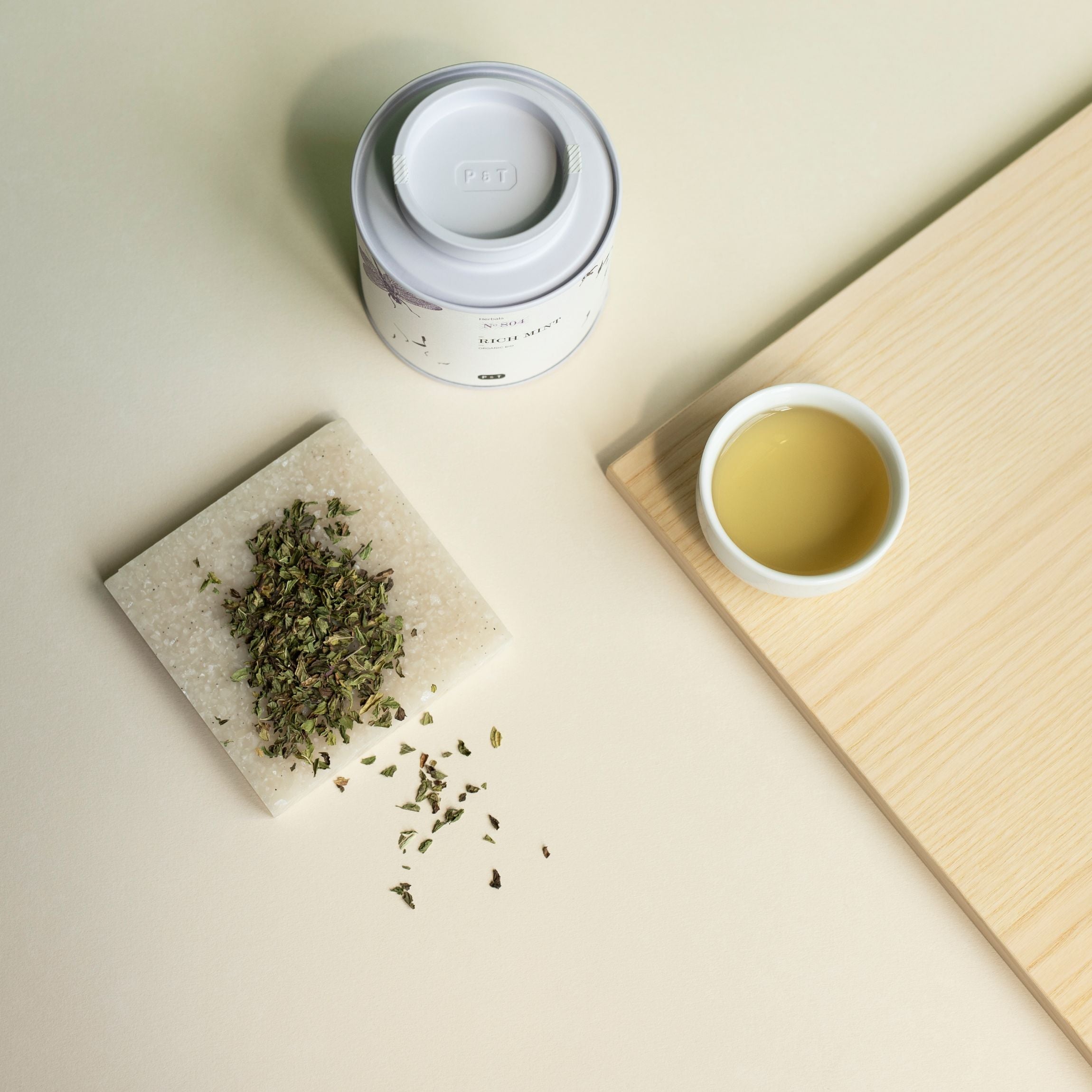Weißer Teebehälter mit Aufschrift P & T No 804 Rich Mint Herbals, weiße Tasse mit Minztee, Holztablett, Minzblätter.