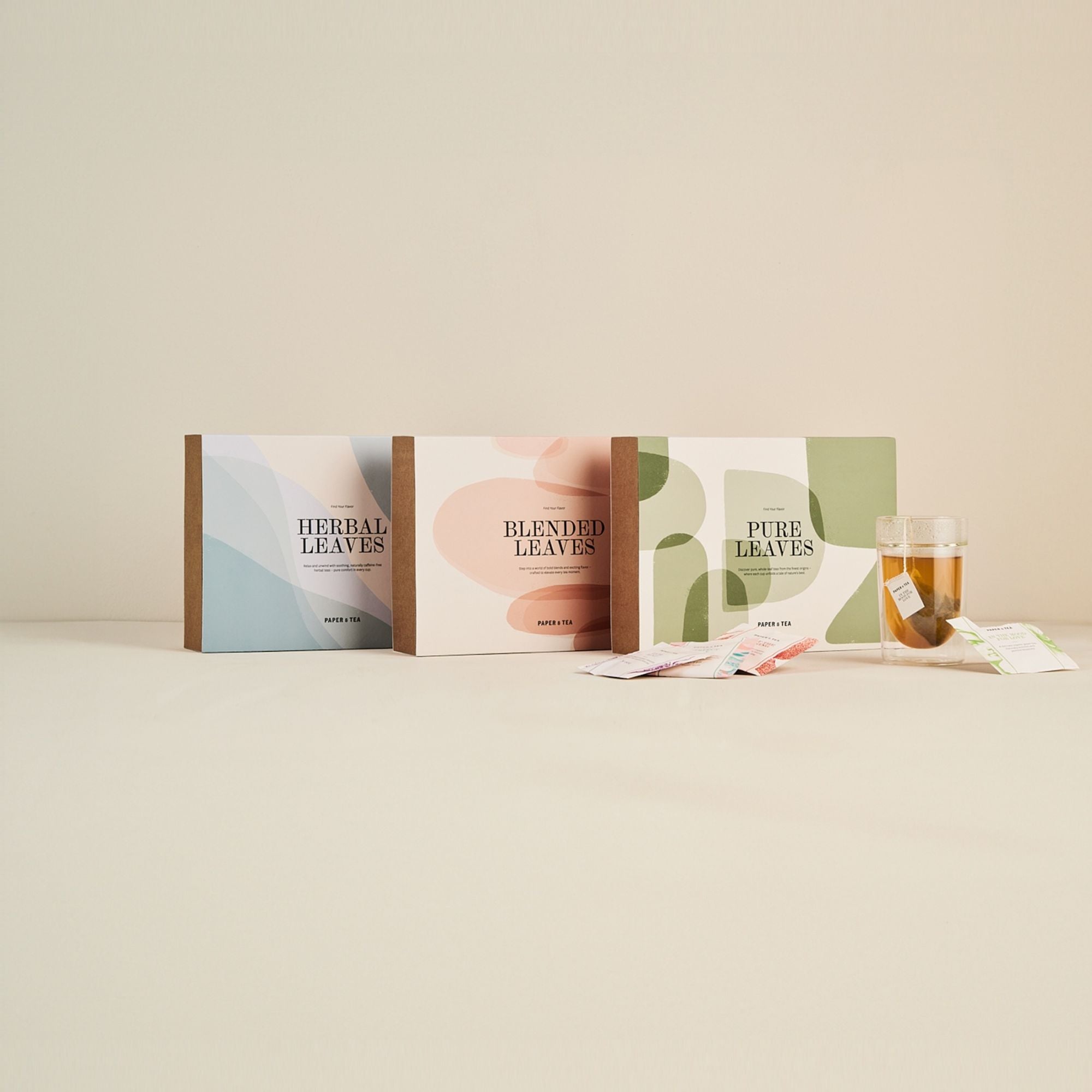 Drei stilvolle Paper & Tea Teeboxen mit Kräuter-, Misch- und reinen Blättern neben frischem Tee.