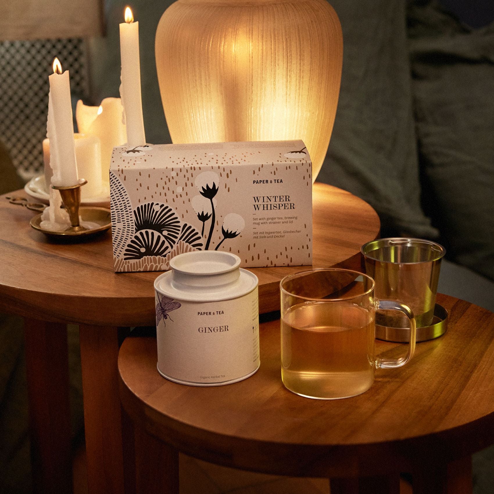 Gemütliche Teeszene mit Winter Whisper Set von PAPER & TEA, Ingwertee, Glasbecher mit Sieb und Kerzenlicht
