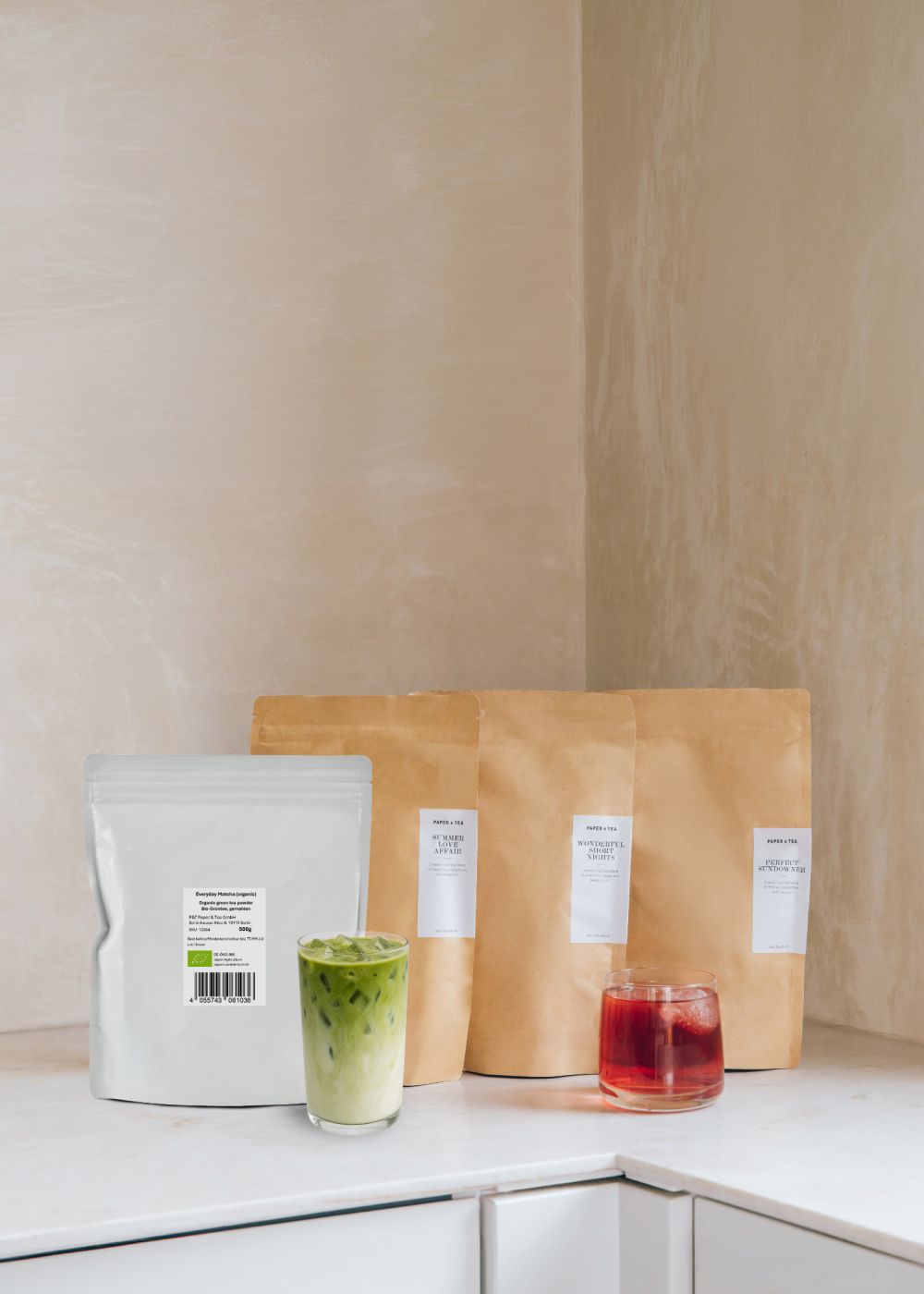 Drei braune P&T Teebeutel, Everyday Matcha Bio-Packung und zwei Eistees auf weißem Marmor in Küche