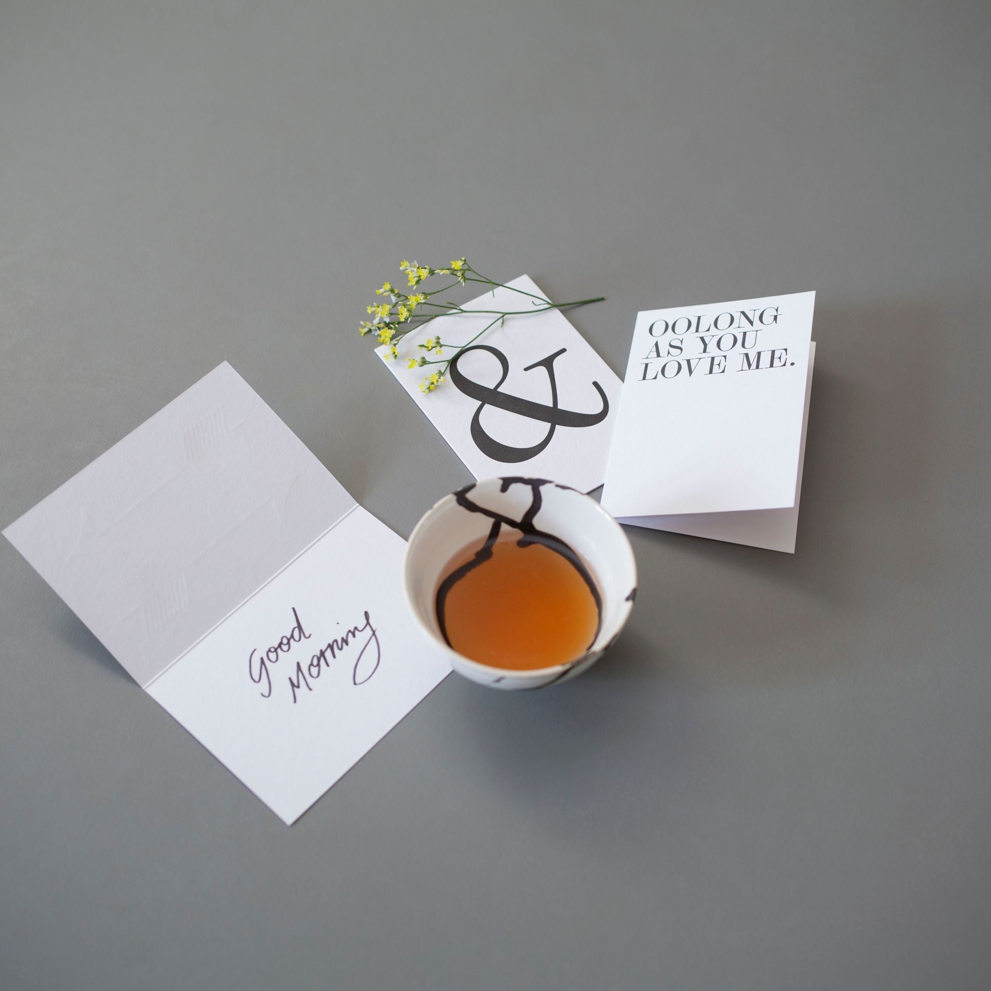 Kunstvoll verzierter Teebecher mit Oolong-Tee neben Grußkarten, dekoriert mit gelben Blümchen.