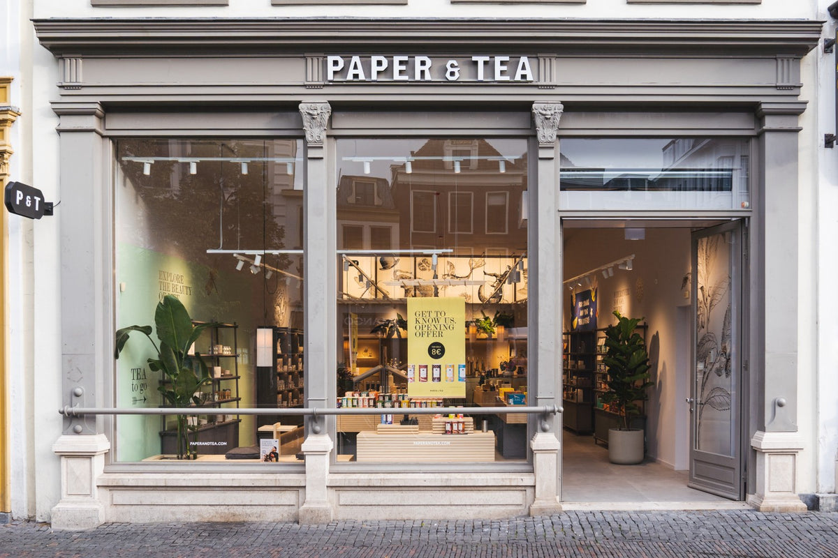 Eleganter Eingang des Paper & Tea Teeladens mit großen Fenstern und Regalen voller Premium-Tees.