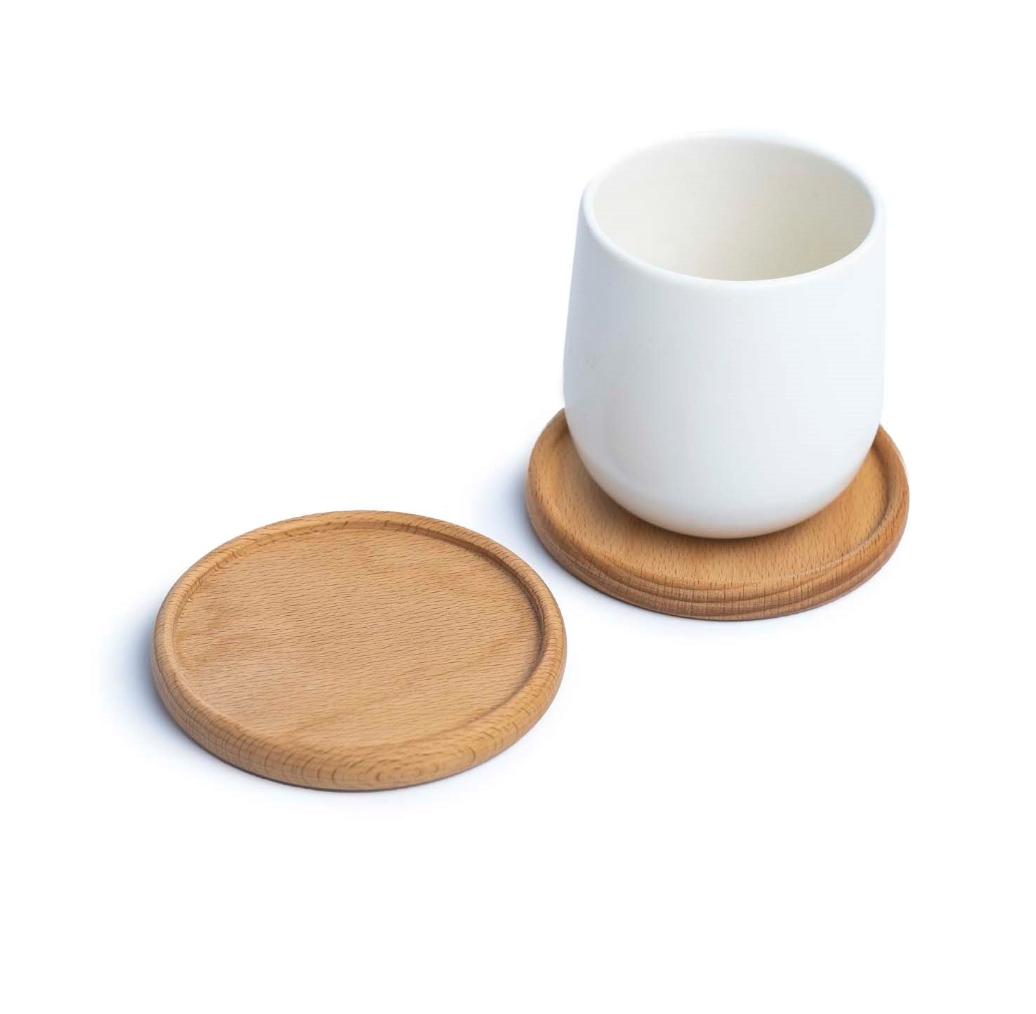 Weiße Teetasse ohne Henkel auf rundem Holzuntersetzer mit sichtbarer Maserung, daneben ein leerer Untersetzer.