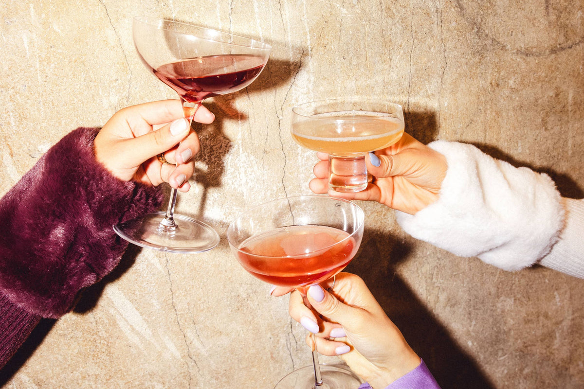 Drei Hände mit gepflegten Nägeln halten bunte Cocktails in einer festlichen Atmosphäre