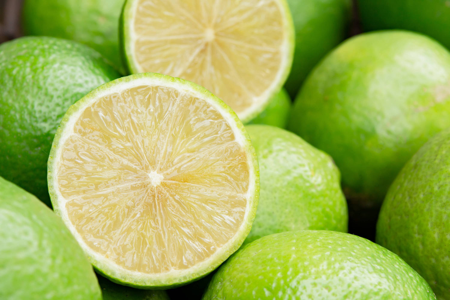 Nahaufnahme einer halbierten Limette, umgeben von grünen Limetten