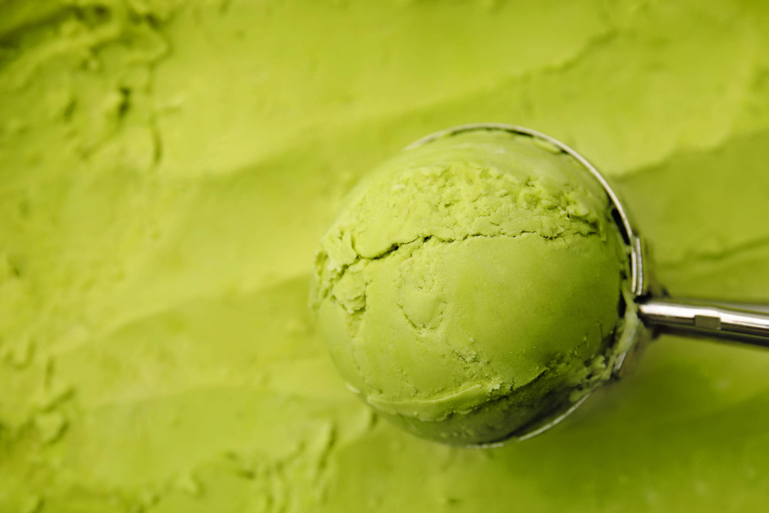 Metall-Eiskugelportionierer mit grünem Matcha-Eis vor Eis im Hintergrund
