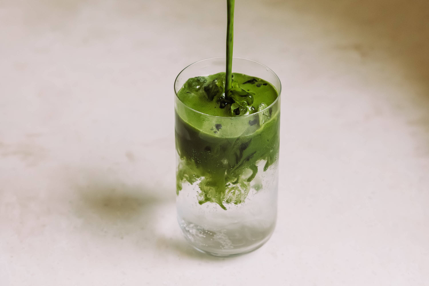 Glas mit Eiswürfeln und grünem Matcha, der sich im klaren Tonic vermischt