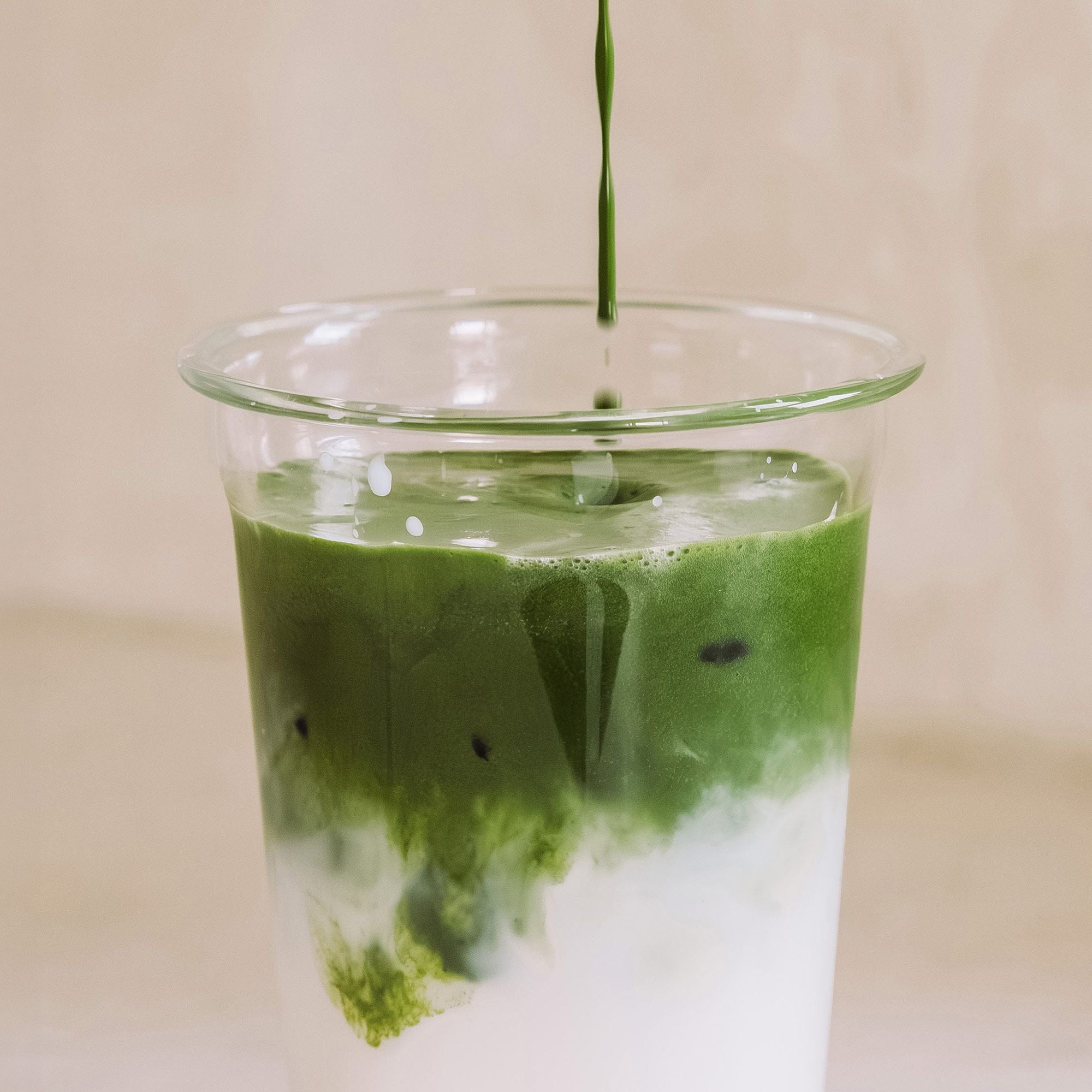 Matcha-Latte im Glas, grüner Matcha über weißer Milch mit sanften Wirbeln