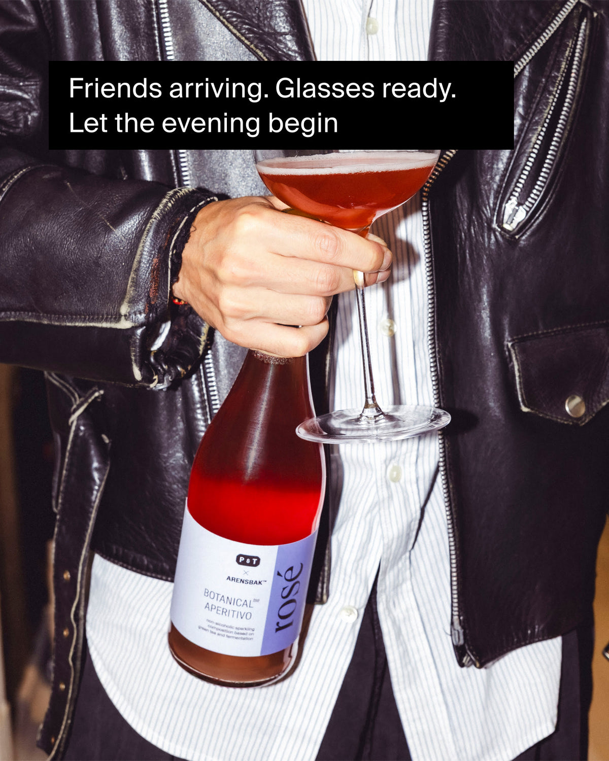 Person hält ein Glas mit roséfarbenem, alkoholfreiem P&T Arensbak Botanical Aperitivo bei einem stilvollen Treffen.