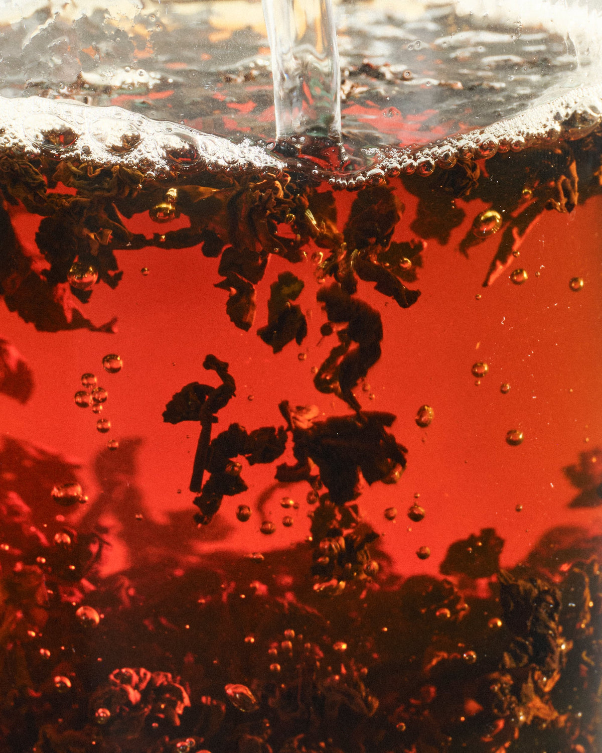 Nahaufnahme eines transparenten Behälters mit dunkelroter Flüssigkeit, in die klares Wasser einfließt.