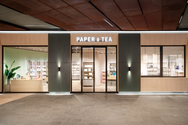Modern gestaltete P&T Filialfassade mit großen Glasfronten, Holzakzenten und grünem Pflanzenarrangement