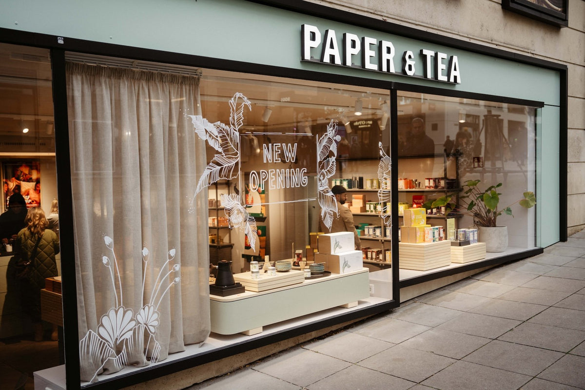P&T Ladenschaufenster mit 'NEW OPENING' und floralen Dekorationen, beige Tische mit Teaprodukten.