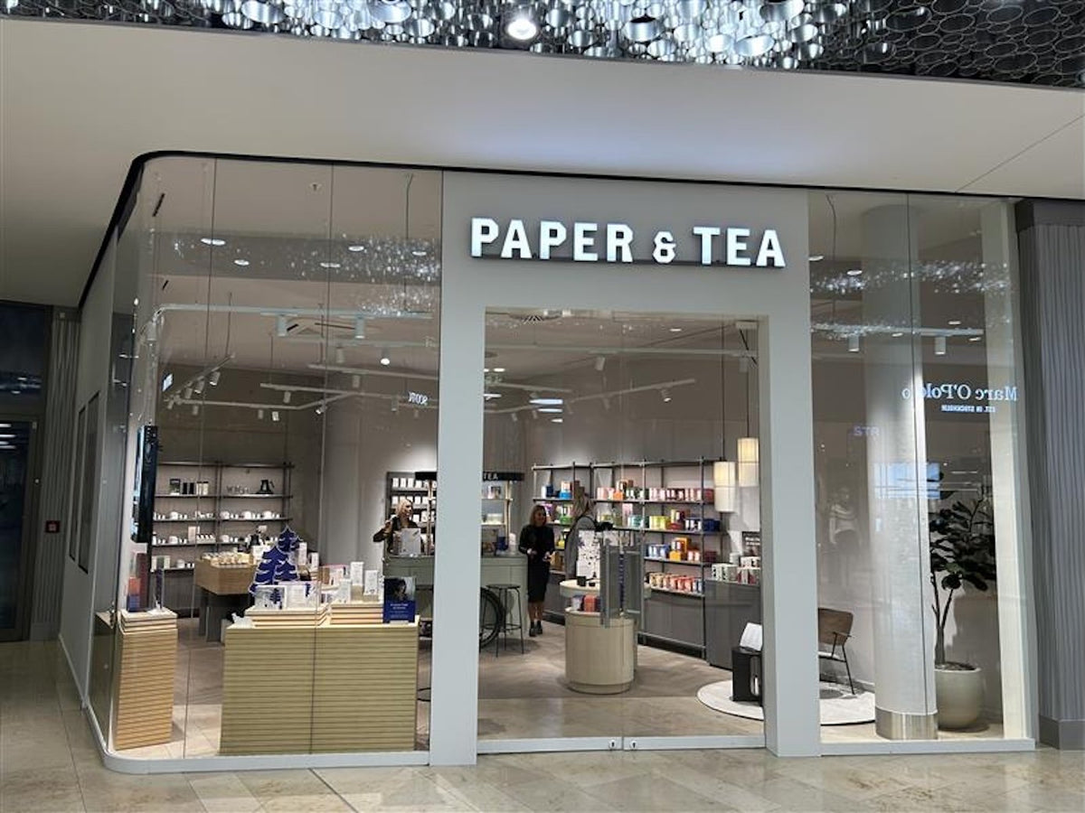 Moderner P&T Laden mit großen Glasfenstern, beleuchtetem Schriftzug und bunten Teeprodukten