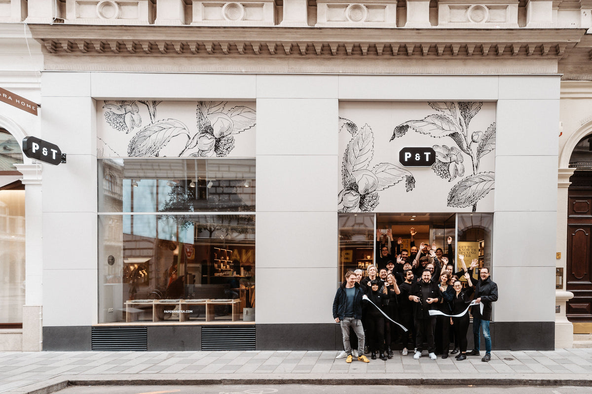 Modernes Paper & Tea Geschäft mit Glasfenstern und botanischen Illustrationen, Eröffnung mit weißem Band.
