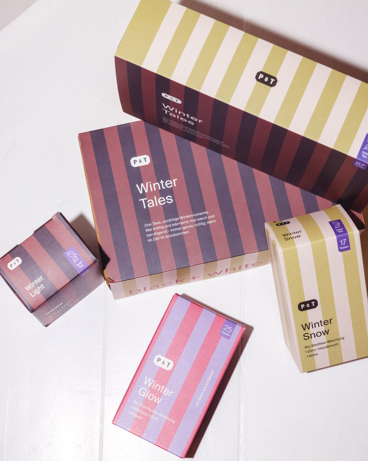 Vier P&T Winter-Teeboxen mit Streifendesign: Winter Tales, Glow, Light und Snow, mit natürlichen Zutaten.